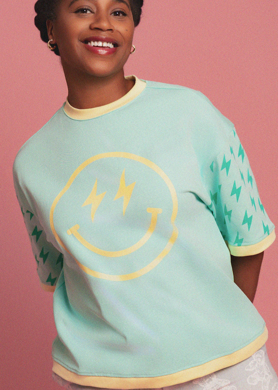 Person wearing a light blue t-shirt with a smiley face design on a pink background