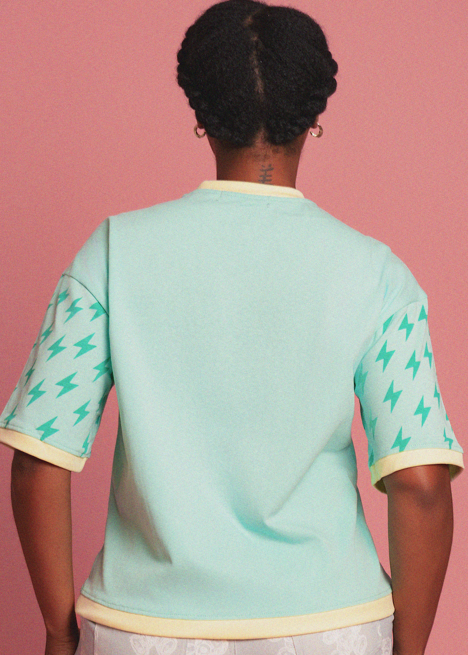 Person wearing a light blue top with green patterns on a pink background
