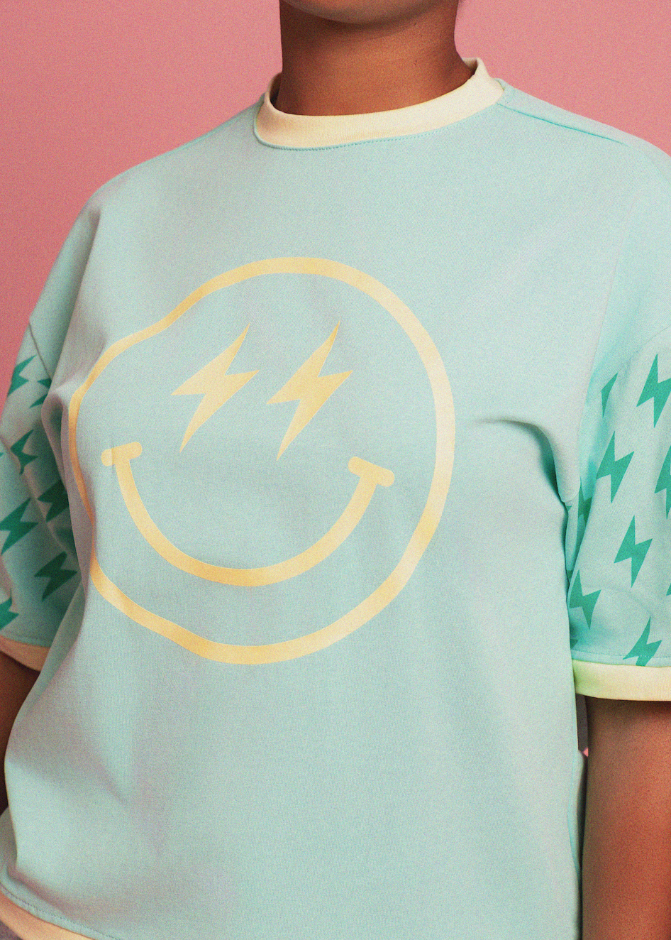 Light blue t-shirt with yellow smiley face design on a pink background