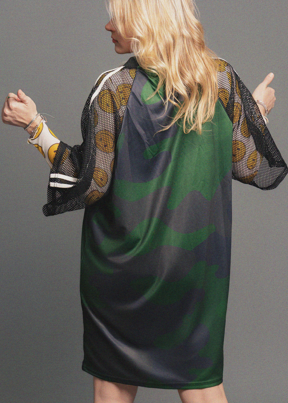 Woman wearing a green and black patterned dress with sheer sleeves against a gray background