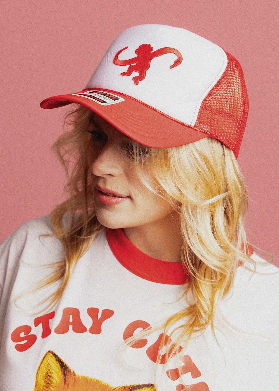 Person wearing a red and white cap with a monkey logo against a pink background