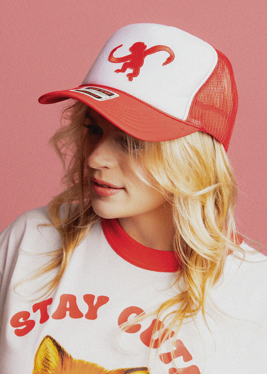 Person wearing a red and white cap with a monkey logo against a pink background