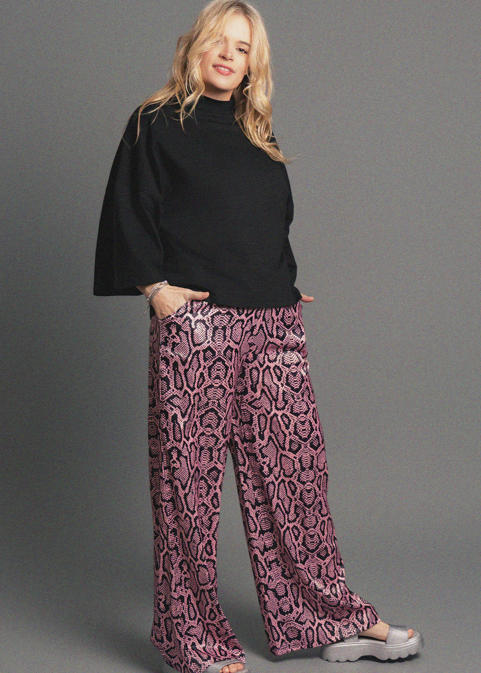 Woman wearing a black top and patterned pants on a gray background