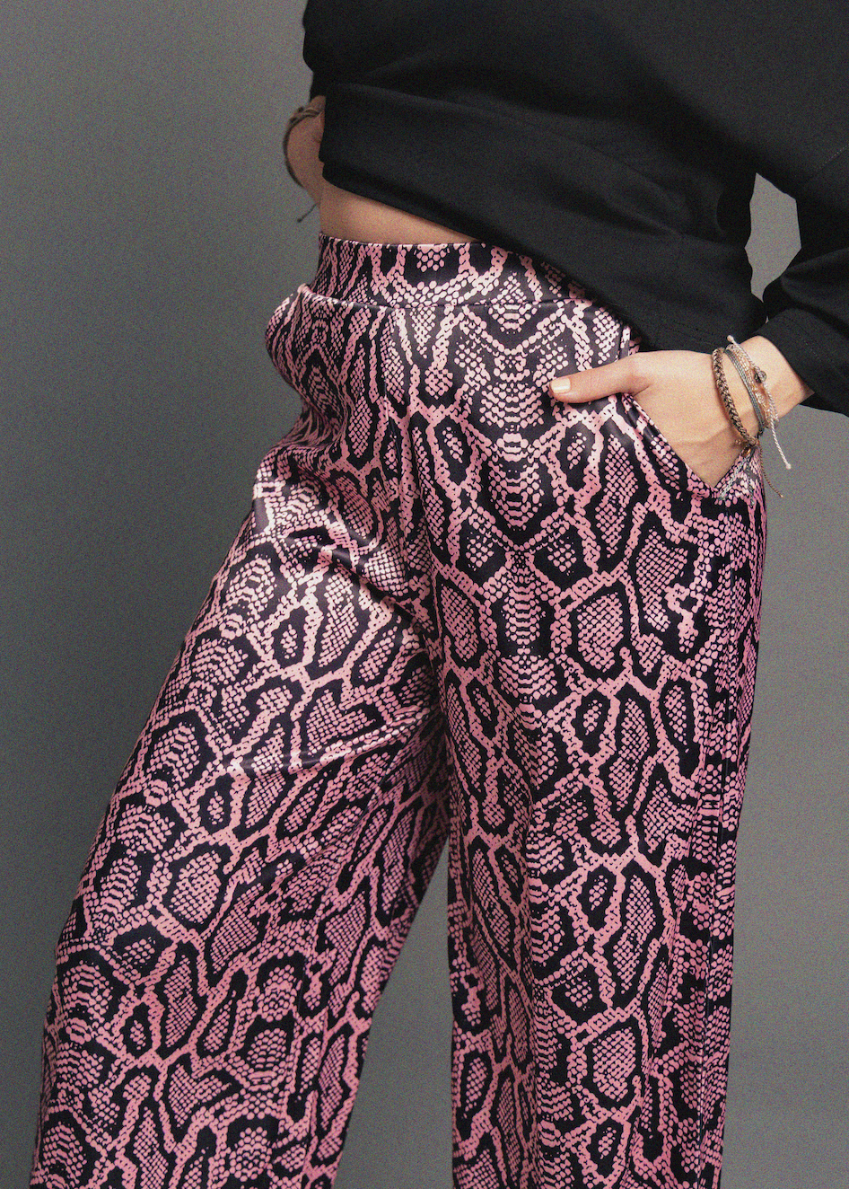 Pink and black patterned pants worn by a person against a gray background