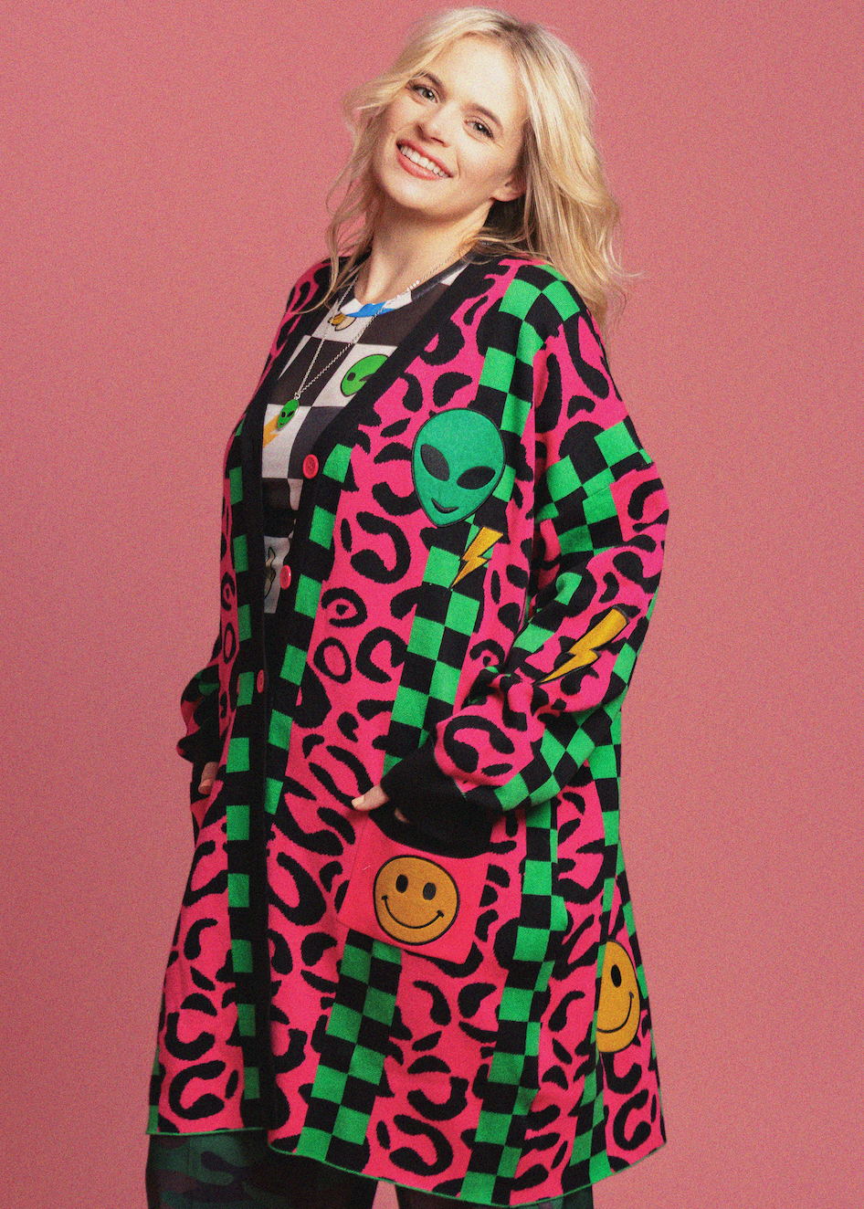 Person wearing a colorful cardigan with checkered and animal print patterns on a pink background