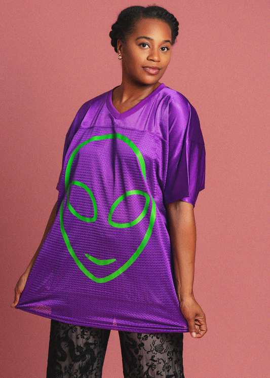 Person wearing a purple jersey with an alien face design on a pink background