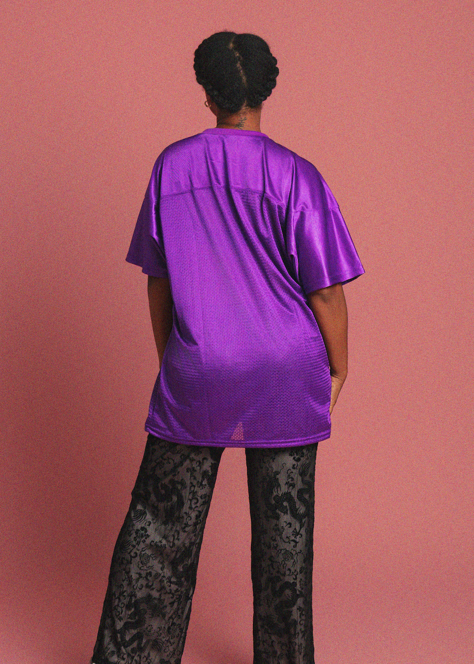 Person wearing a purple shirt and black patterned pants against a pink background