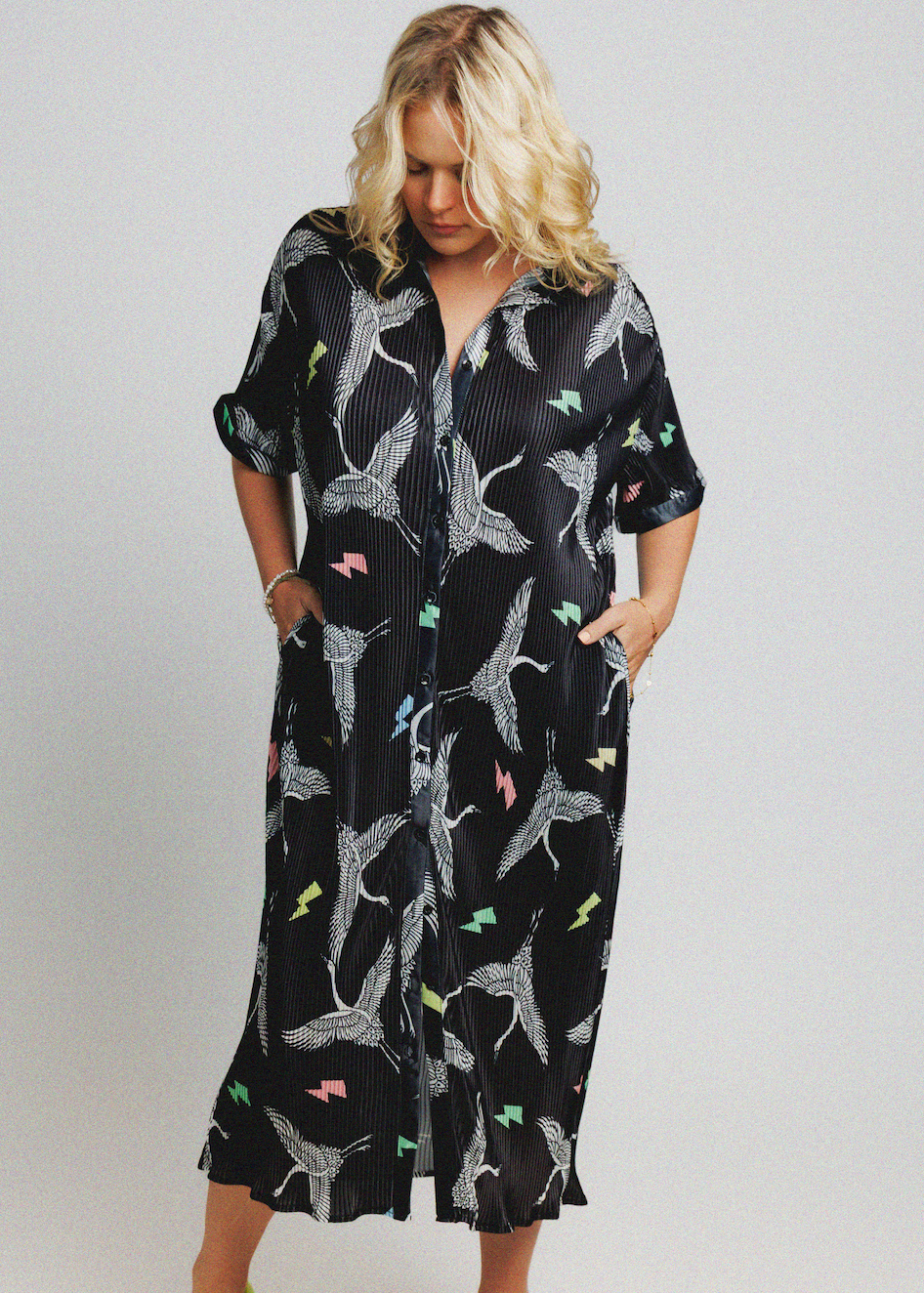 A woman modeling a black midi shirt dress with a white bird print and small colorful accents, set against a plain light gray background.