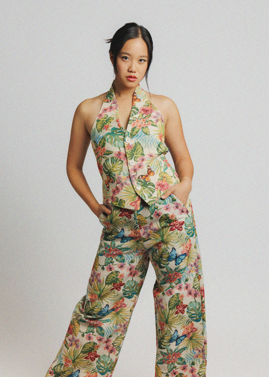 A model wearing a sleeveless halter vest and matching wide-leg pants set in a tropical floral print, posed against a light gray studio background.