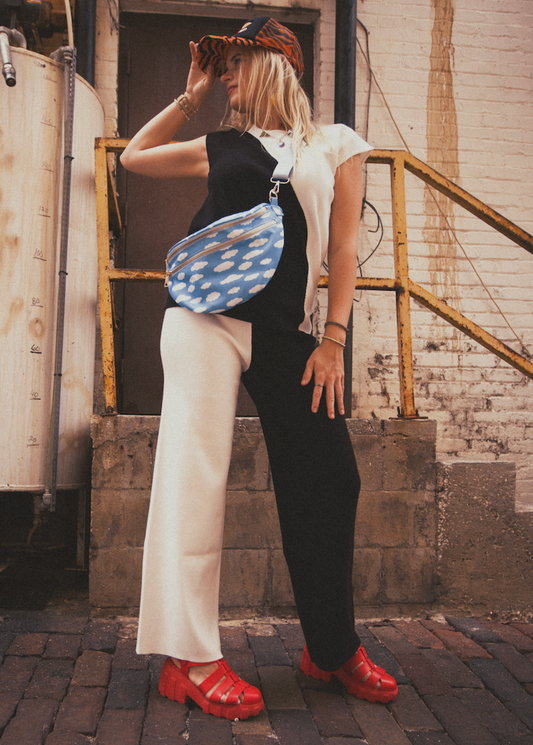 Person wearing a black and white top, black and white pants, red shoes, and a blue cloud print bag in an urban setting.