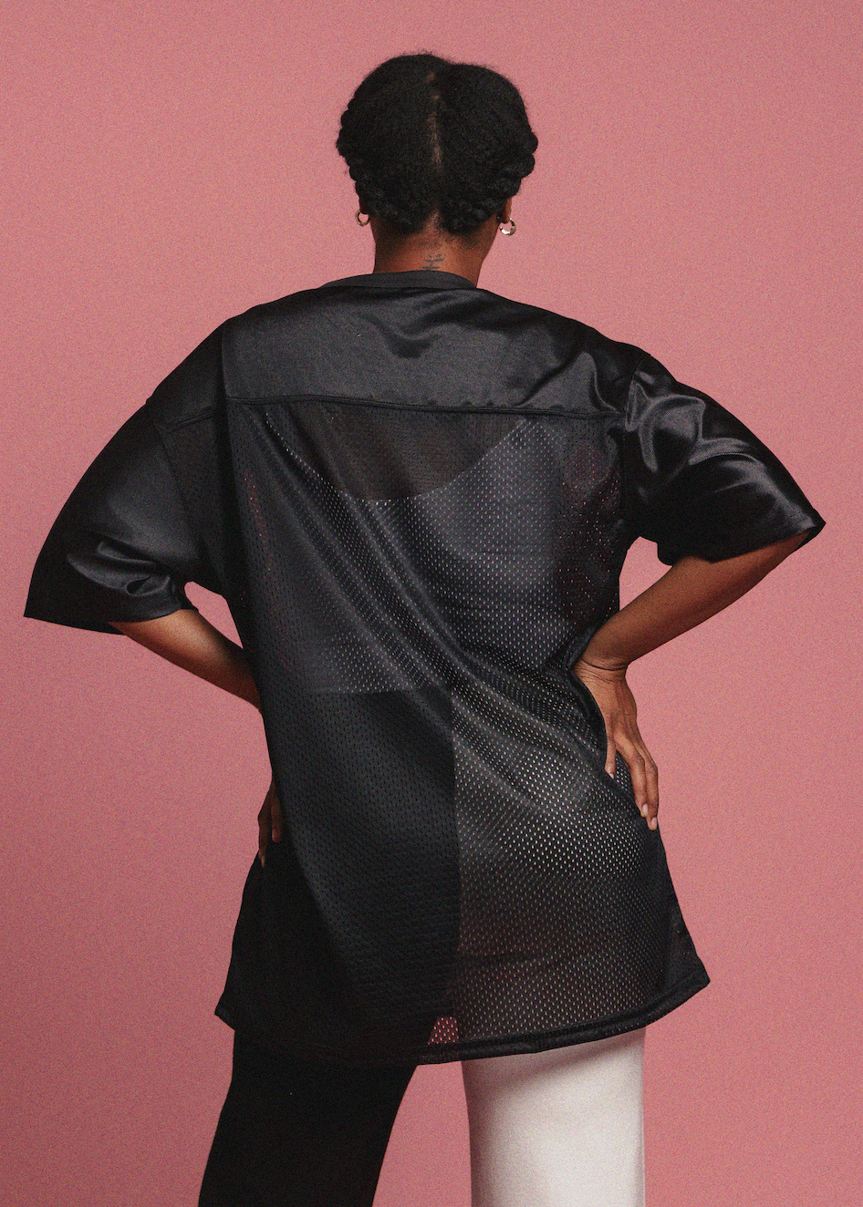 Person wearing a black outfit with geometric pattern on a pink background