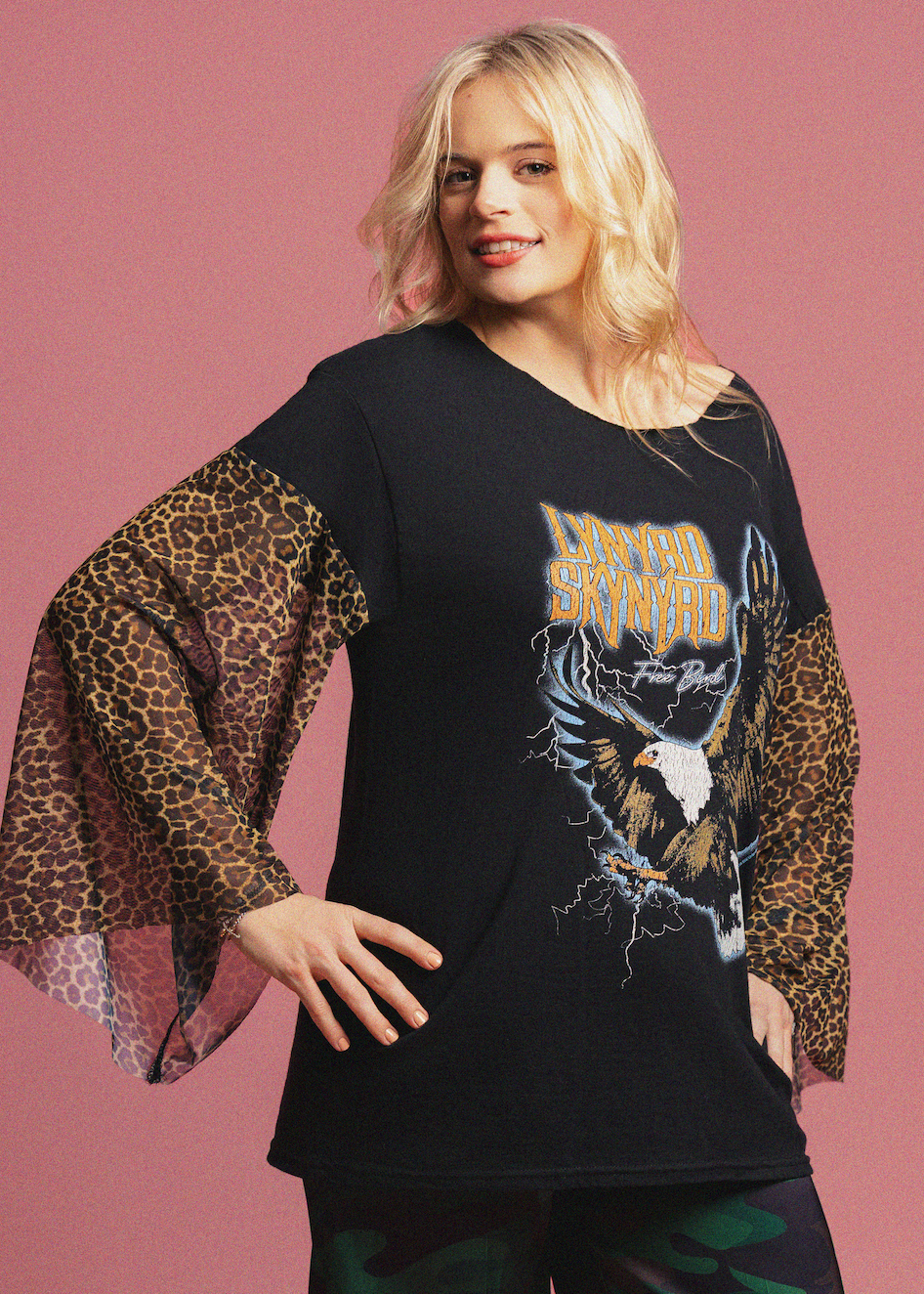 Woman wearing a black shirt with a graphic design and leopard sleeves on a pink background