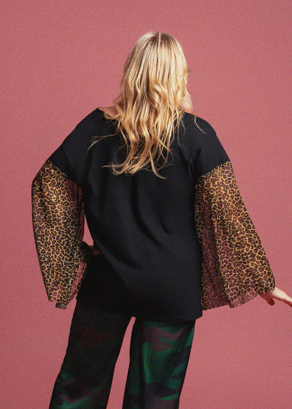 Person wearing a black top with leopard print sleeves against a pink background