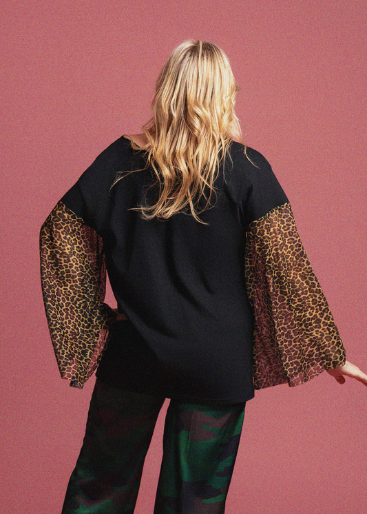 Person wearing a black top with leopard print sleeves against a pink background