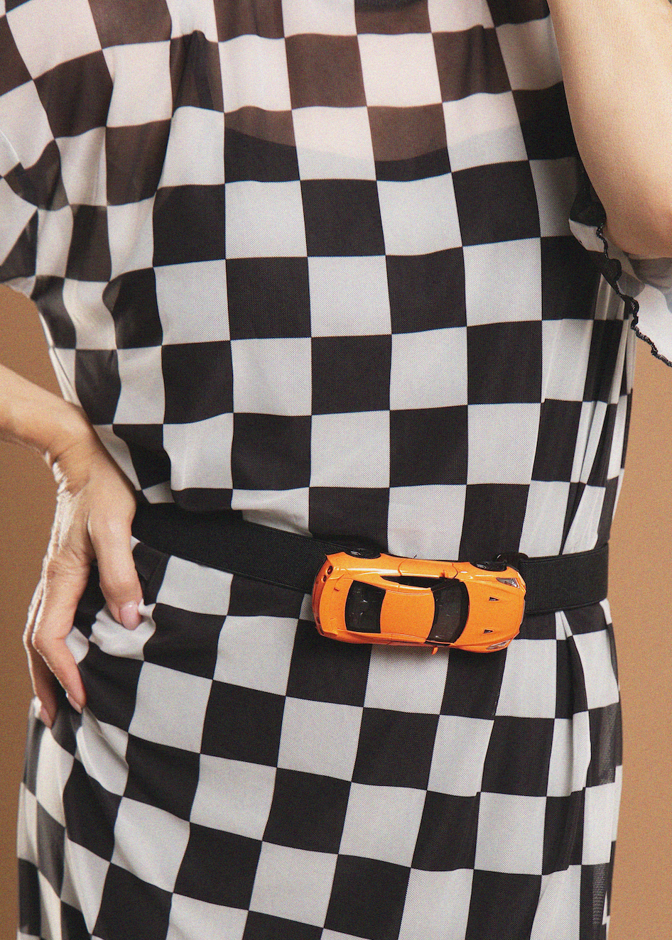 A close-up of a person wearing a black and white checkered dress with a black belt and an orange toy car buckle.
